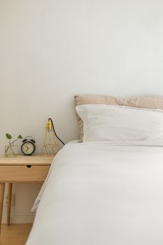 Clean and cozy minimalist bedroom featuring white bedding and modern decor on a wooden bedside table.