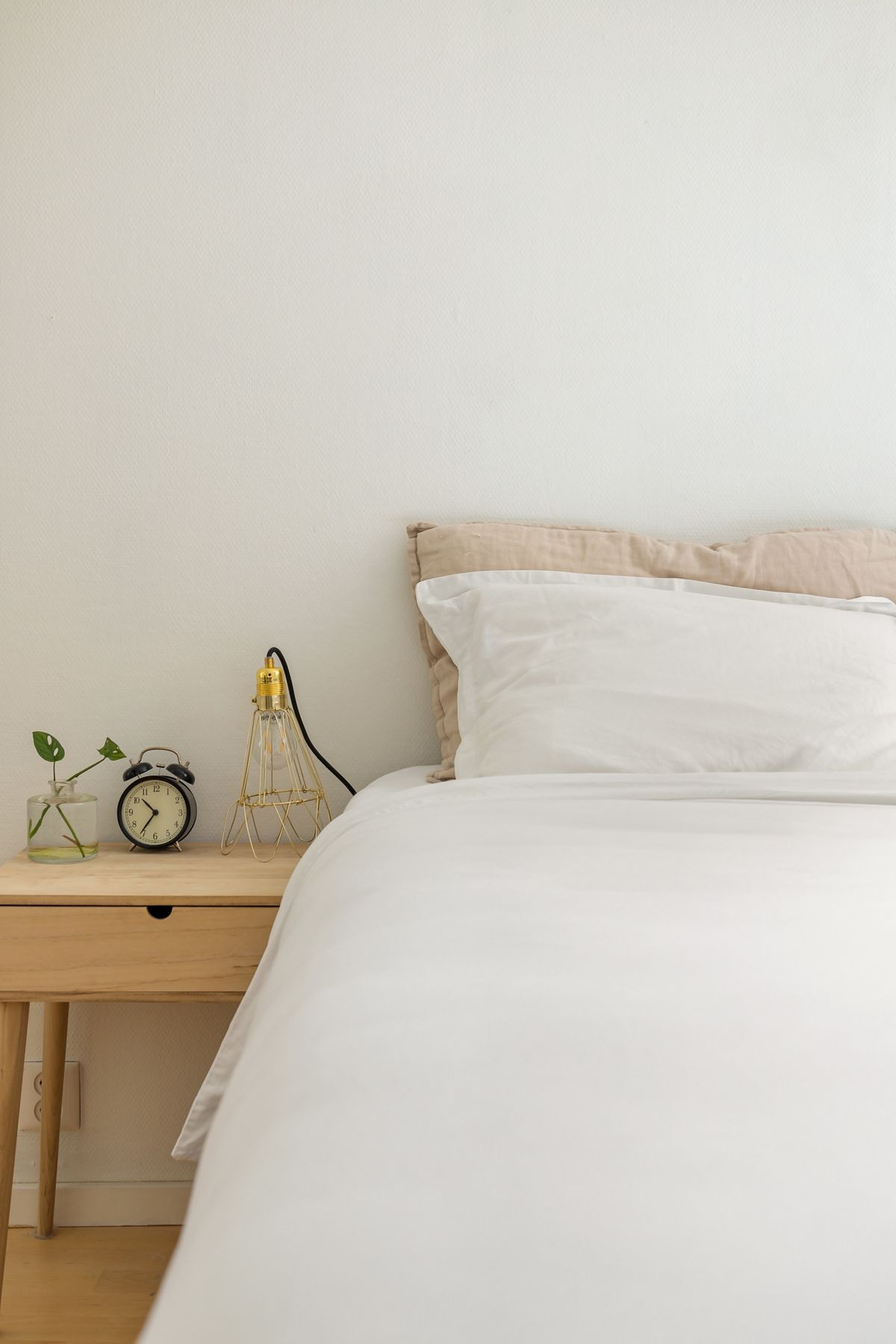 Serene minimalist bedroom with a bed, white linens, wooden bedside table, lamp, and neutral decor