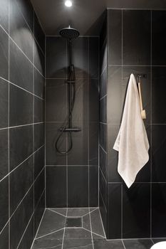 Minimalist black tiled shower with hanging white towel and modern fixtures.