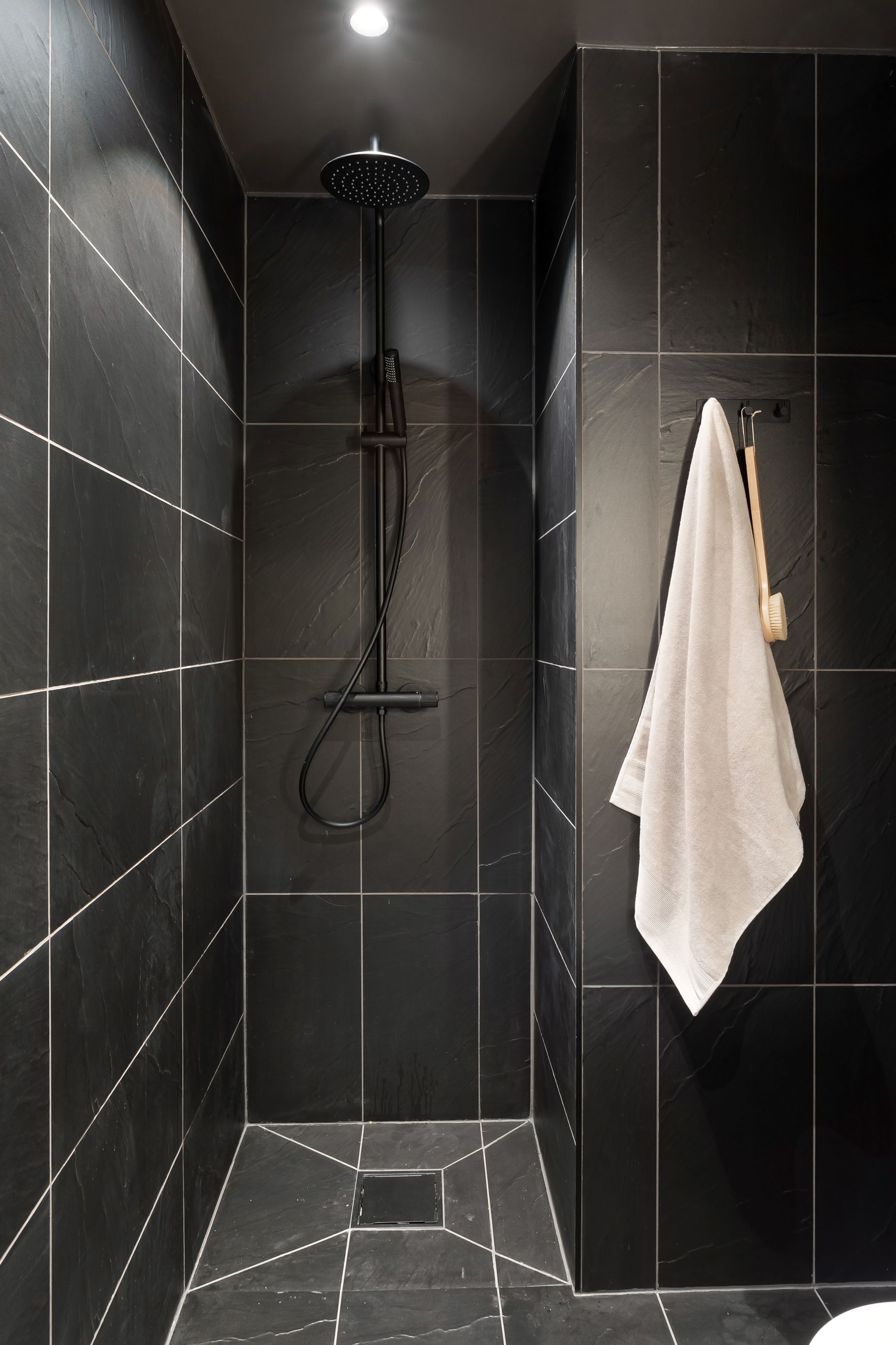 Black tiled shower with white towel and sleek dark fixtures