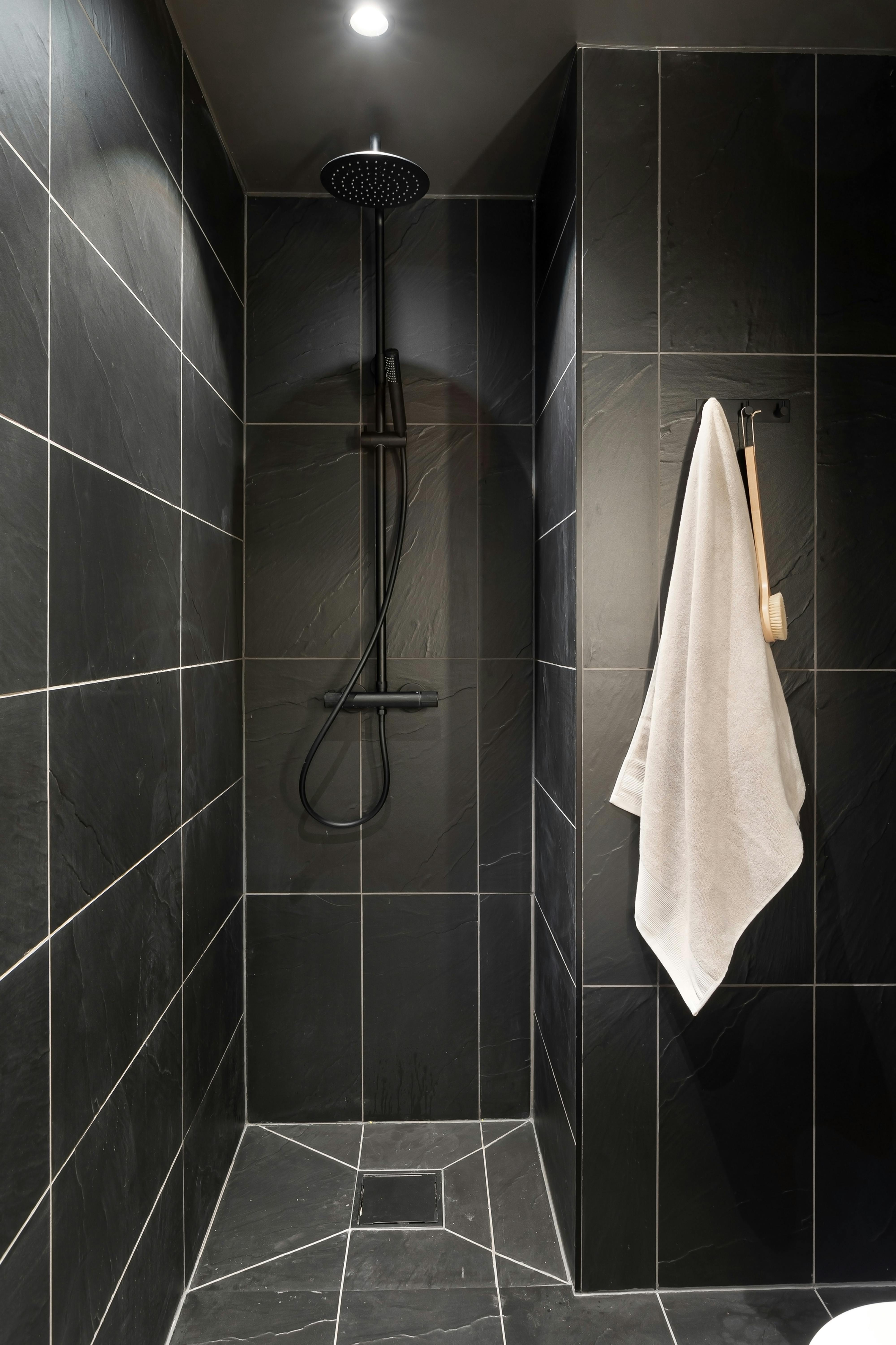 Free Minimalist black tiled shower with hanging white towel and modern fixtures. Stock Photo