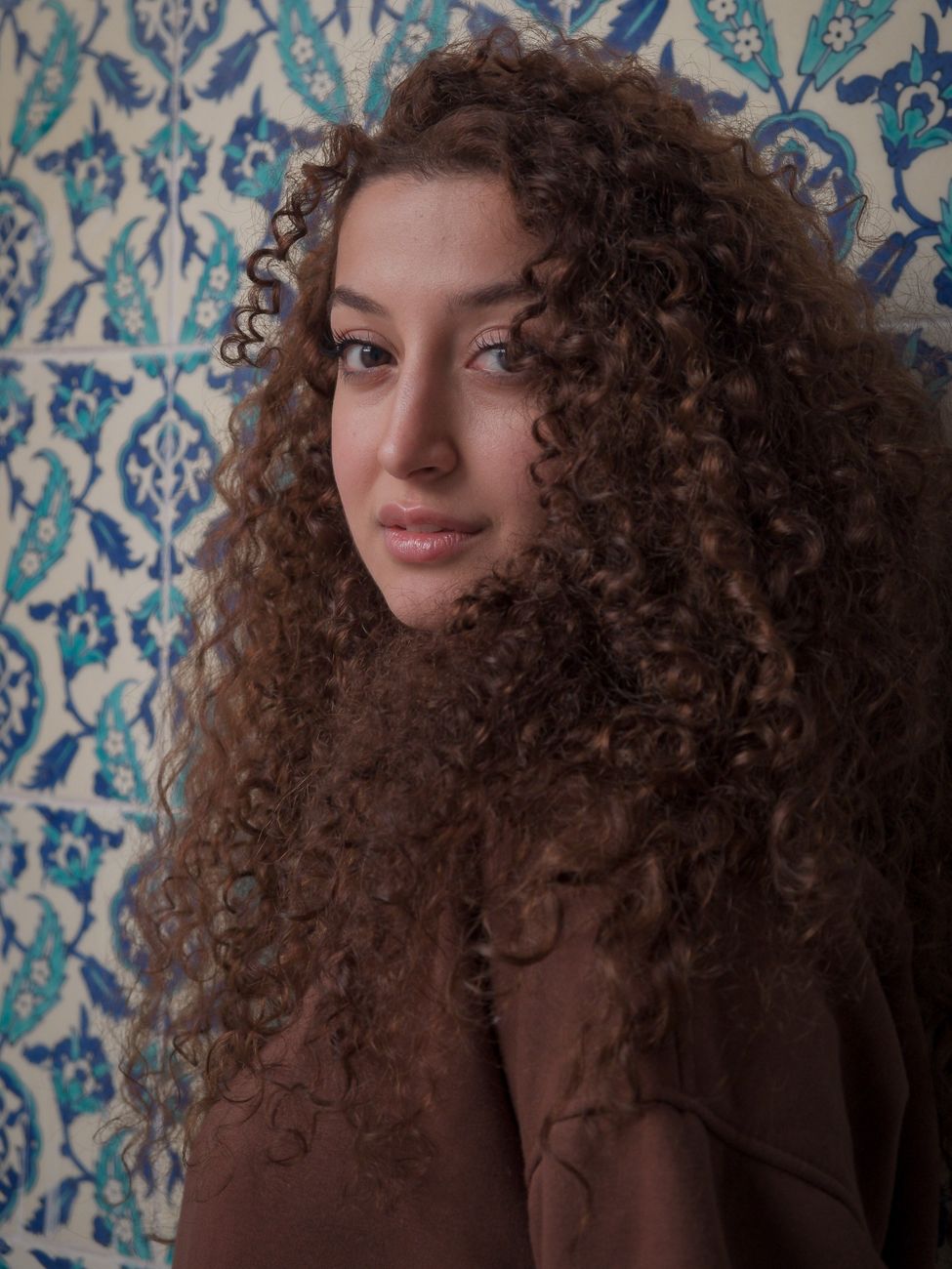 Elegant portrait of a woman with curly hair against traditional İstanbul tiles.