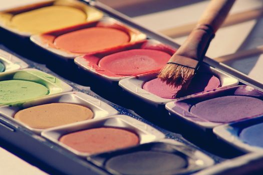 Close-up of a colorful watercolor palette with a paintbrush ready for artistic creation.