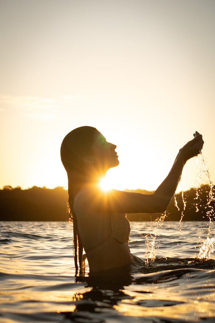 Woman In Bikini Splashing Water At Sunset