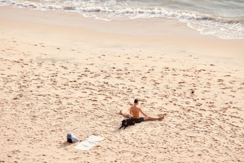 Man Sitting with Dog and Stretching on Beach