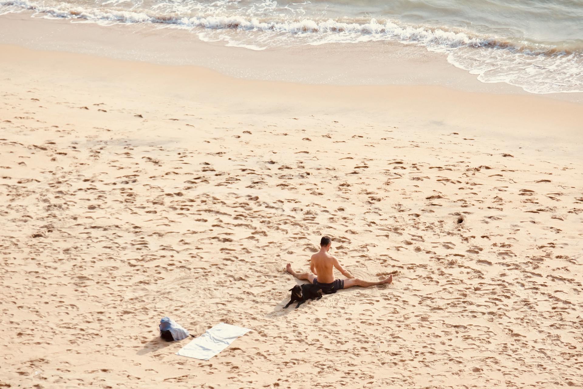 Man Sitting with Dog and Stretching on Beach