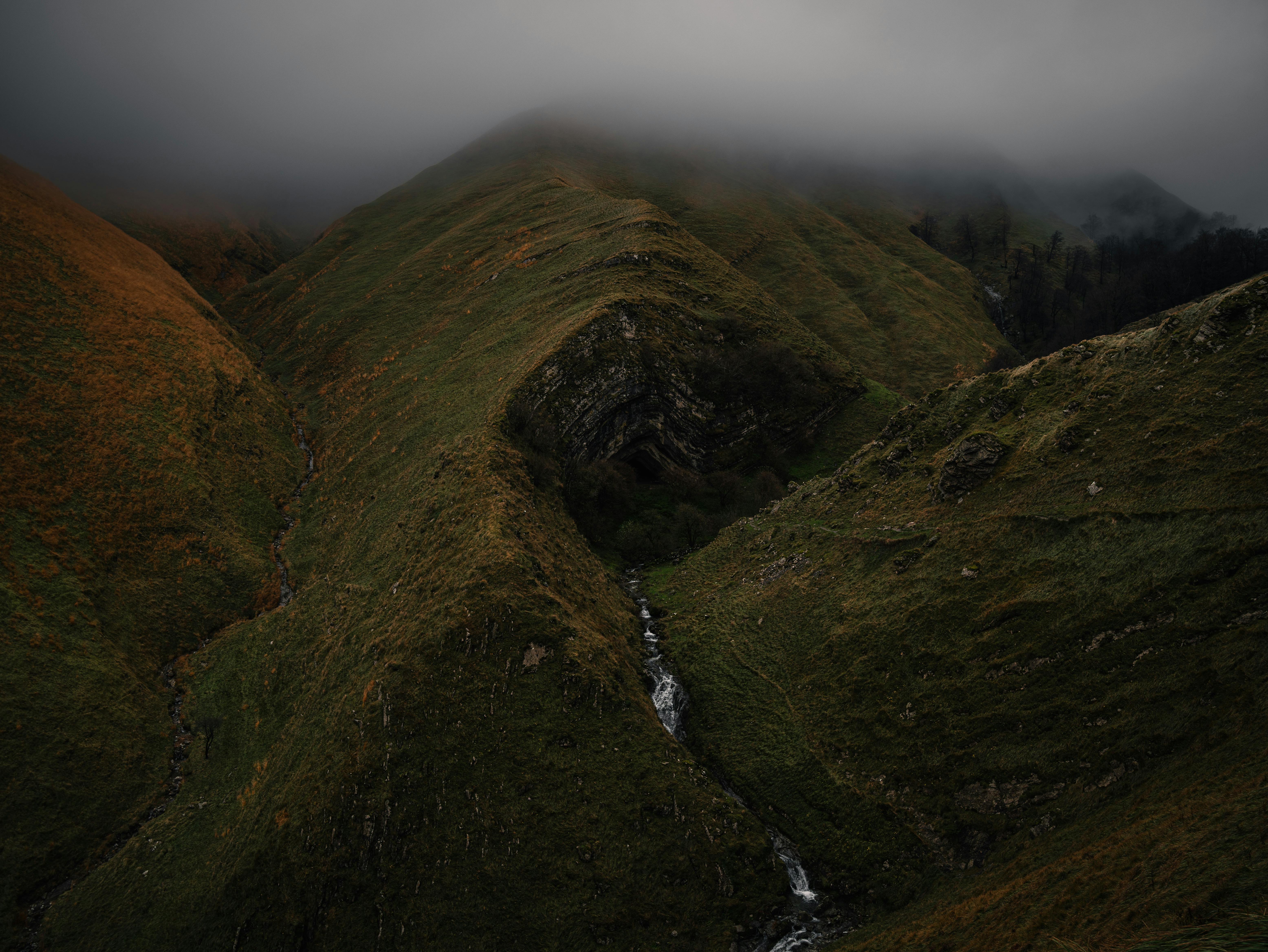 Moody mountain scene featuring lush green hills and dense cloud cover, creating a dramatic atmosphere.