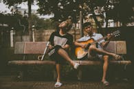 两个年轻人在户外享受音乐表演，一个弹着吉他，另一个则放松身心