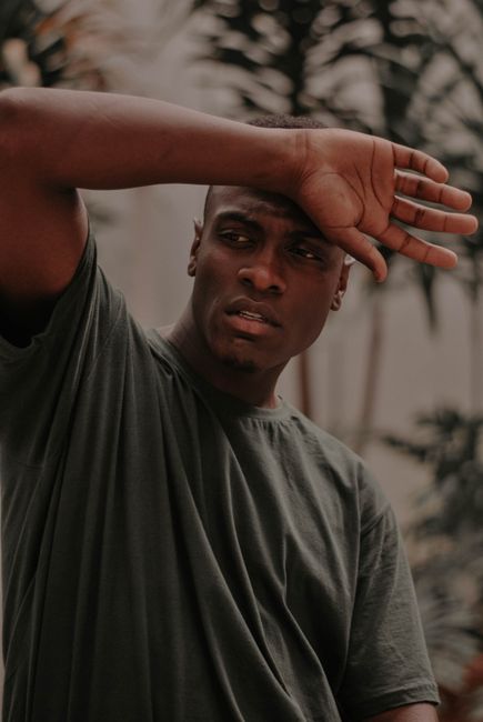 Portrait of a man in a green t-shirt with hand raised, looking away thoughtfully.