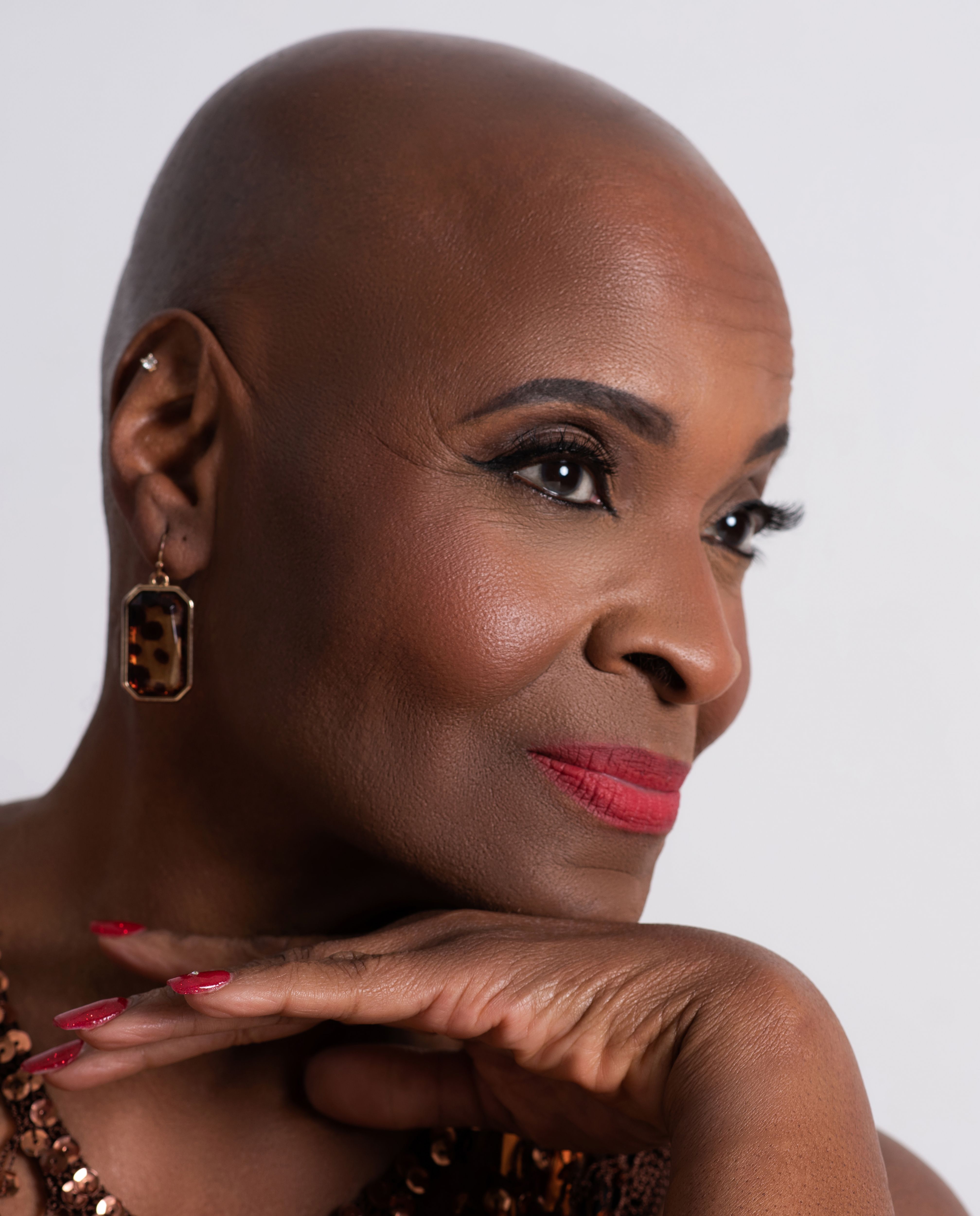 Sophisticated profile portrait of a bald African American woman with red lipstick and earrings.