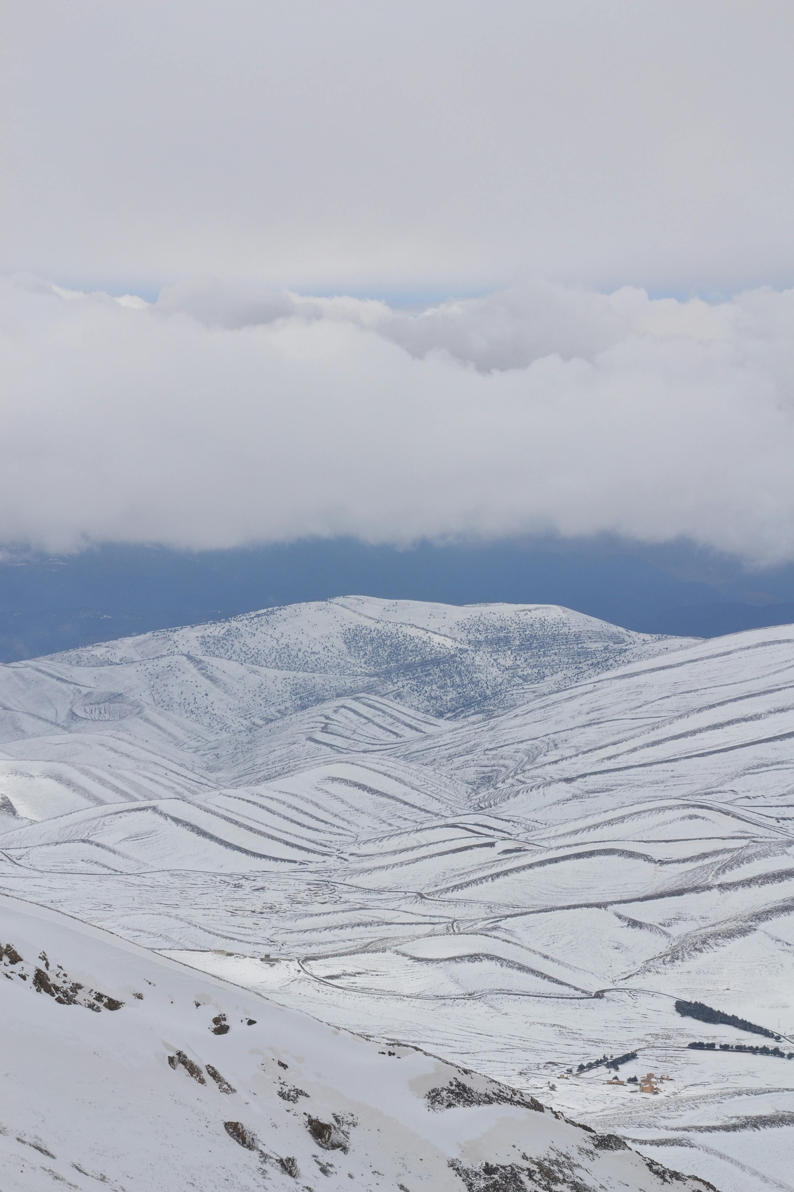 A tranquil winter scene with snow-covered hills and a cloudy sky in an aerial perspective.