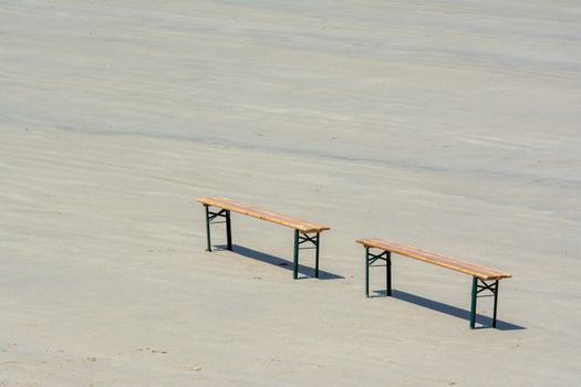 A minimalist photo of two solitary wooden benches on a tranquil beach.