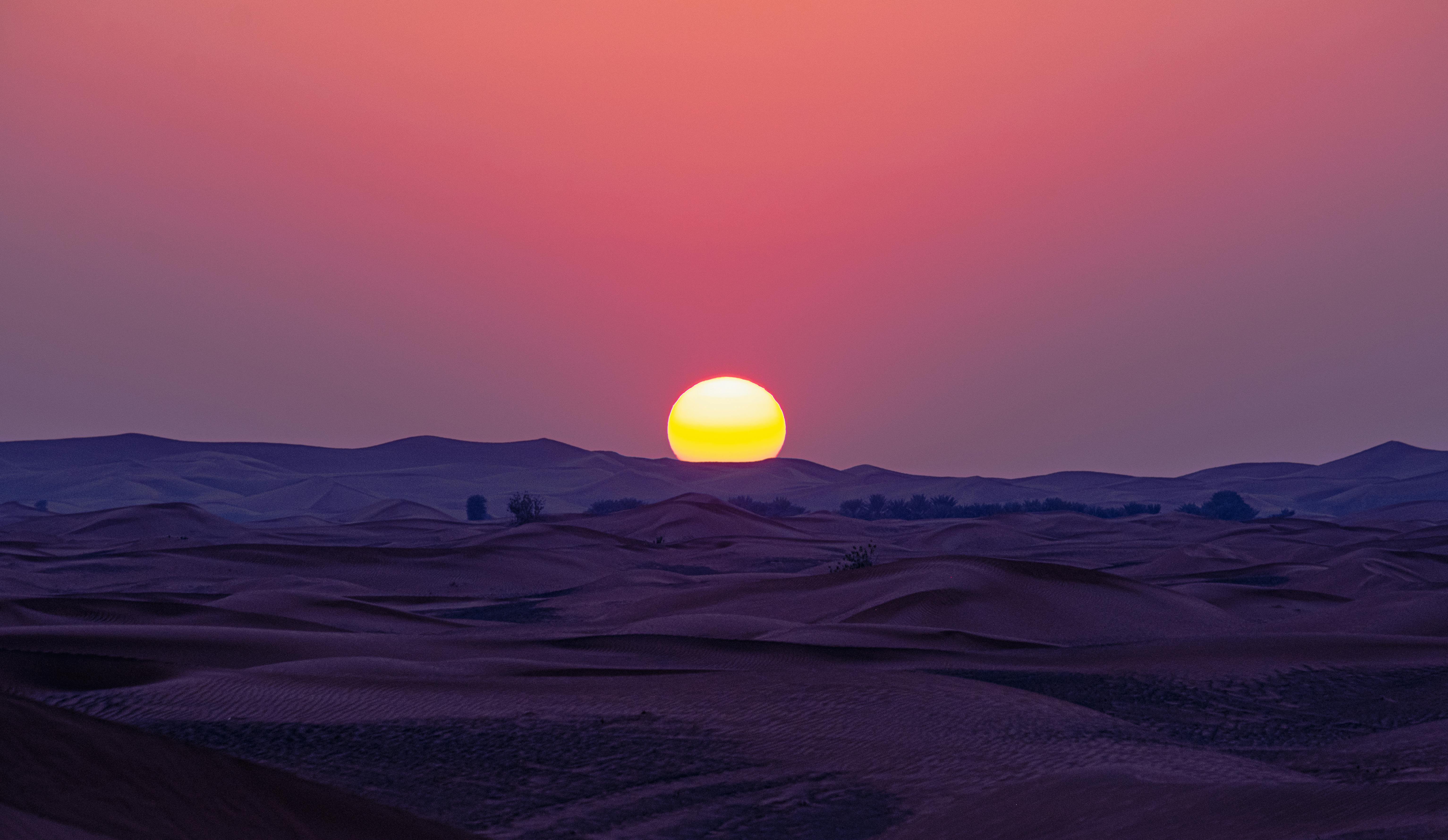 A breathtaking sunset casts vibrant colors over peaceful desert dunes, creating a serene landscape.