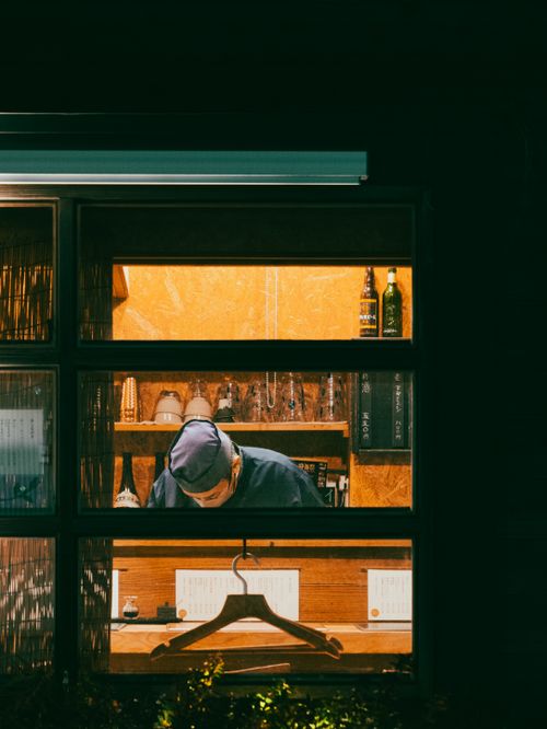 Free A man in a traditional Japanese café viewed from outside at night, focusing on the interior setting and ambiance. Stock Photo