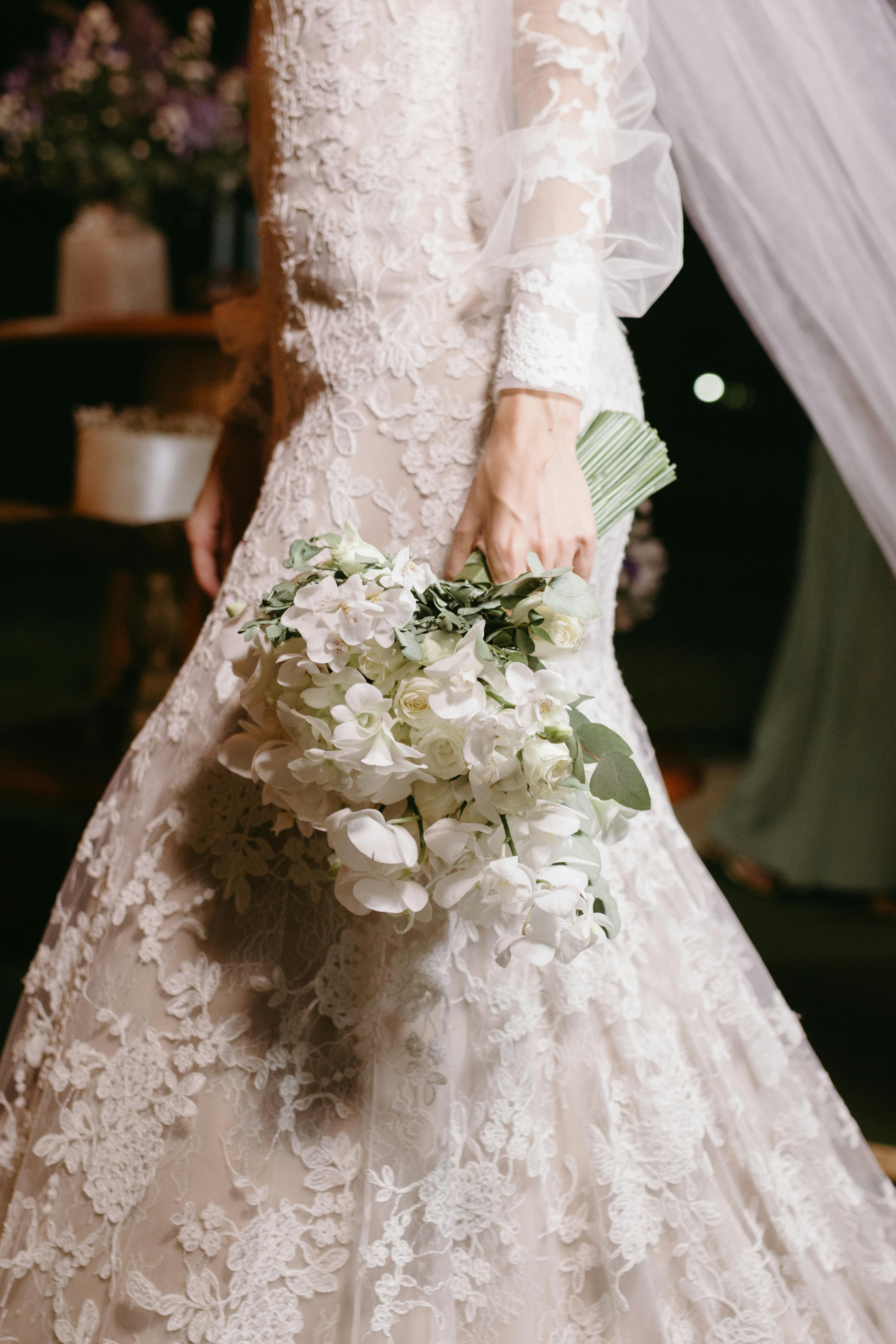 Close-up of a bride in a lace gown holding a white bouquet, showcasing wedding elegance.