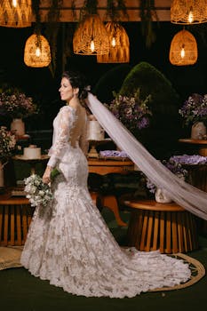 Beautiful bride in lace gown with floral bouquet at evening wedding reception.