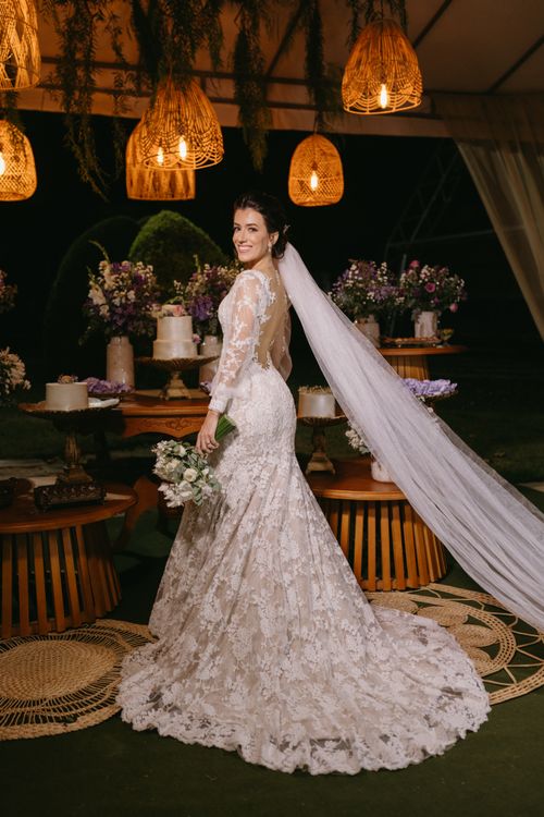 Free A beautiful bride in a lace gown with a long veil stands in a warmly lit wedding setting. Stock Photo