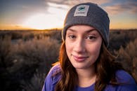 一位年轻女子戴着无檐帽，在日落时分的户外微笑着