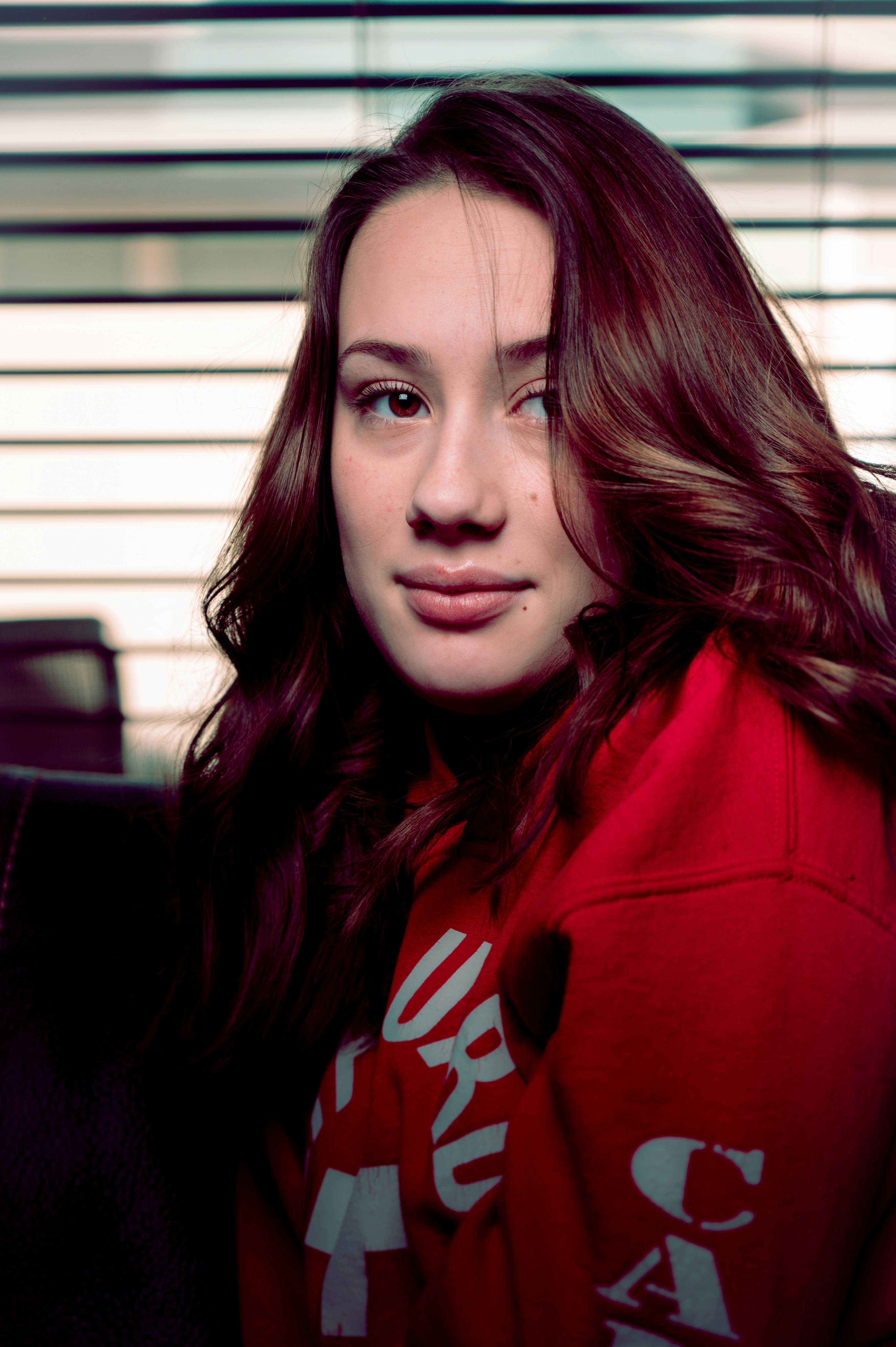 这是一幅年轻女子的肖像，她留着长发，身穿红色毛衣，背景为条纹图案，整体散发着优雅的气息