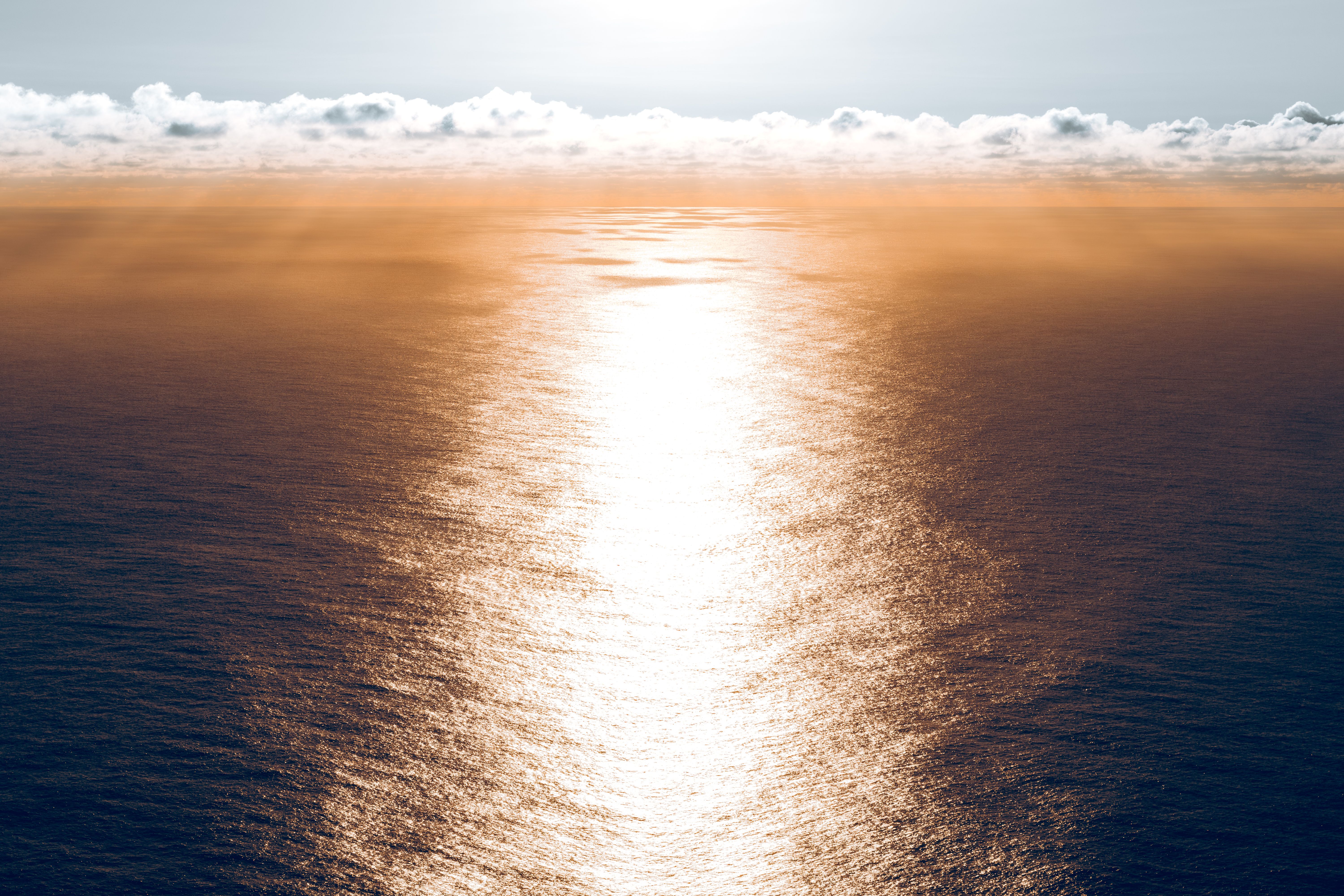 A serene aerial view capturing the sunlit ocean at sunset with calm waters and distant clouds.
