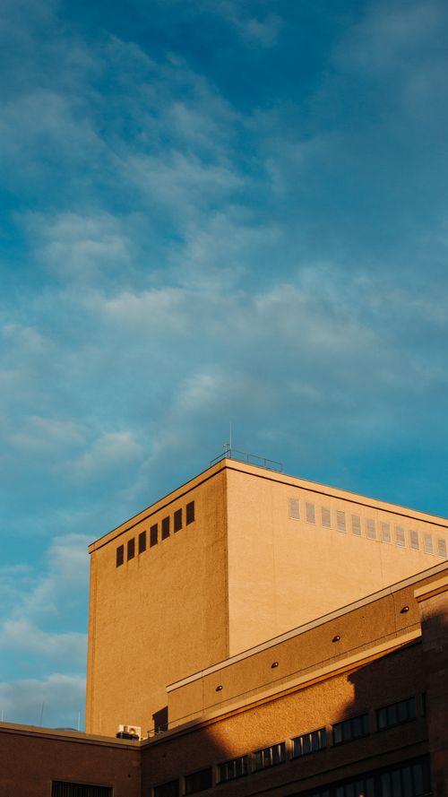 Free Modern building architecture with a yellow facade against a blue sky in Berlin. Stock Photo