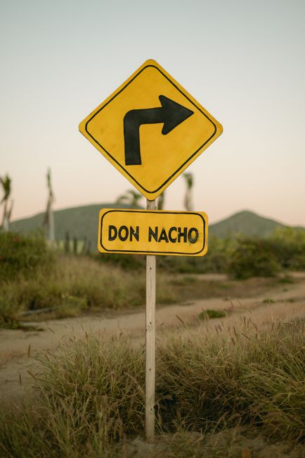Yellow road sign with arrow and 'Don Nacho' in a desert landscape at sunset.