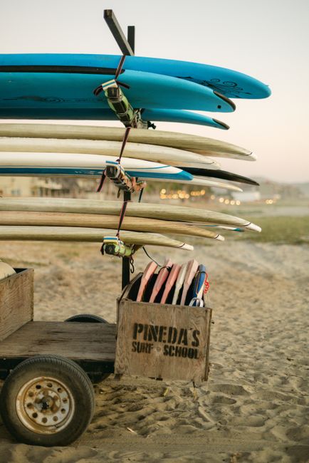 Surfboards on a trailer at a sandy beach during sunset, perfect for surf schools.