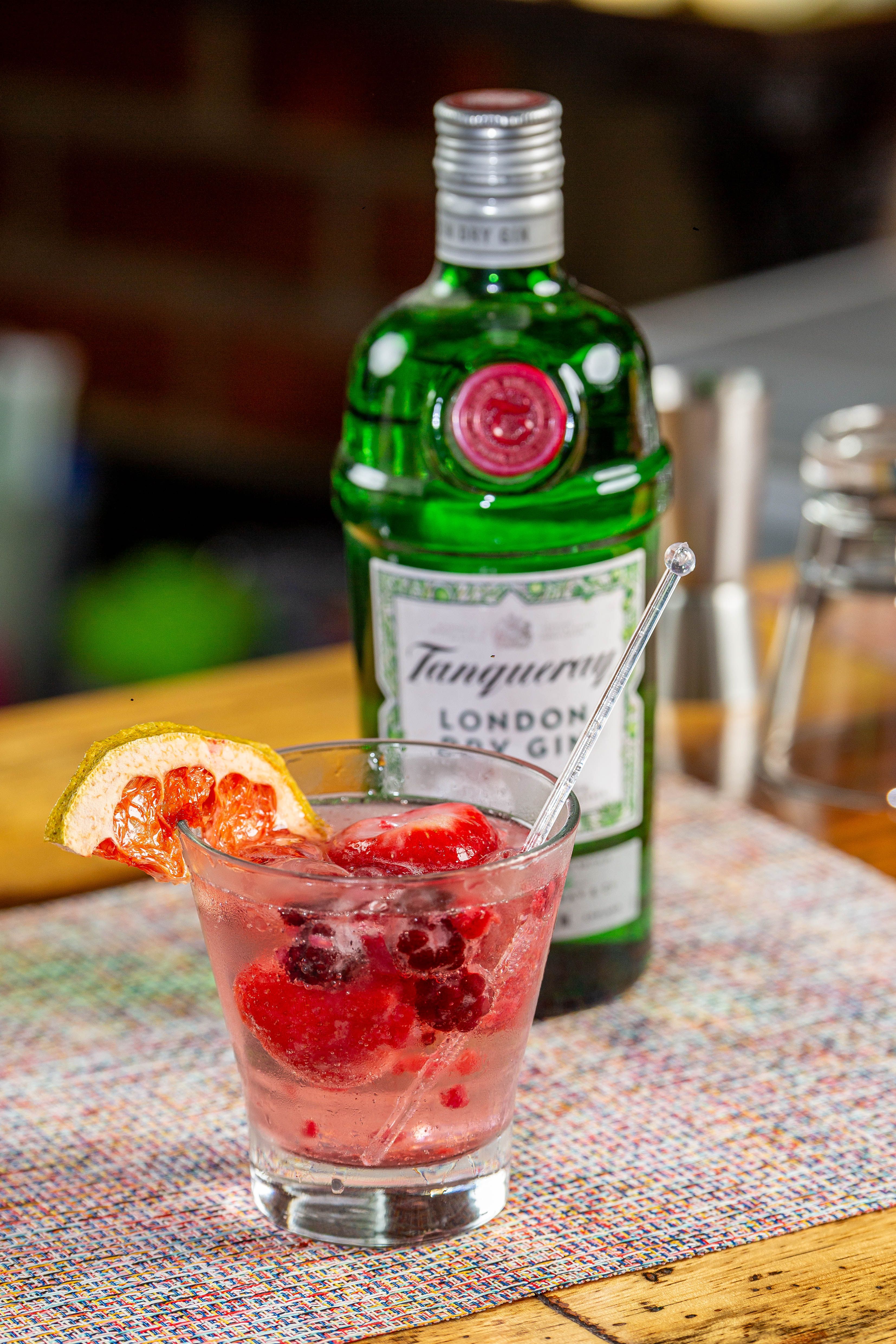 A vibrant gin cocktail with berries and a citrus slice garnished on the rim.