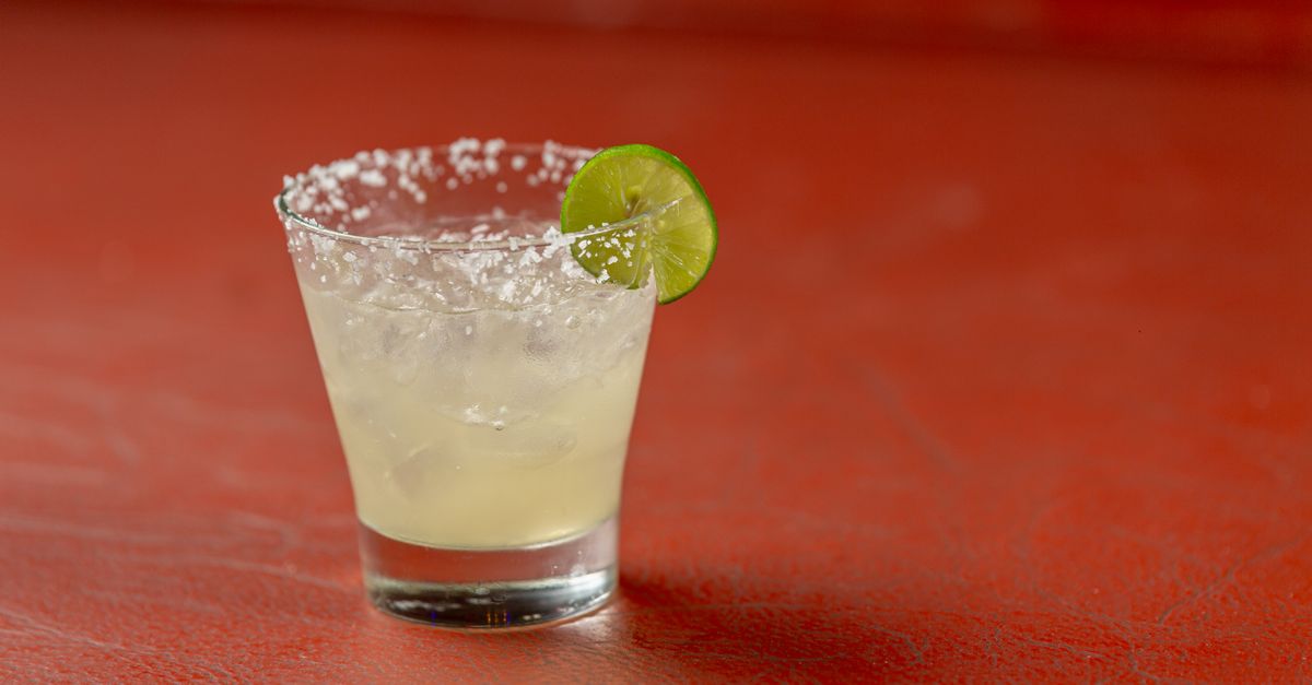 A classic margarita cocktail with lime, salt rim, on a textured red background, perfect for cocktail or summer themes.