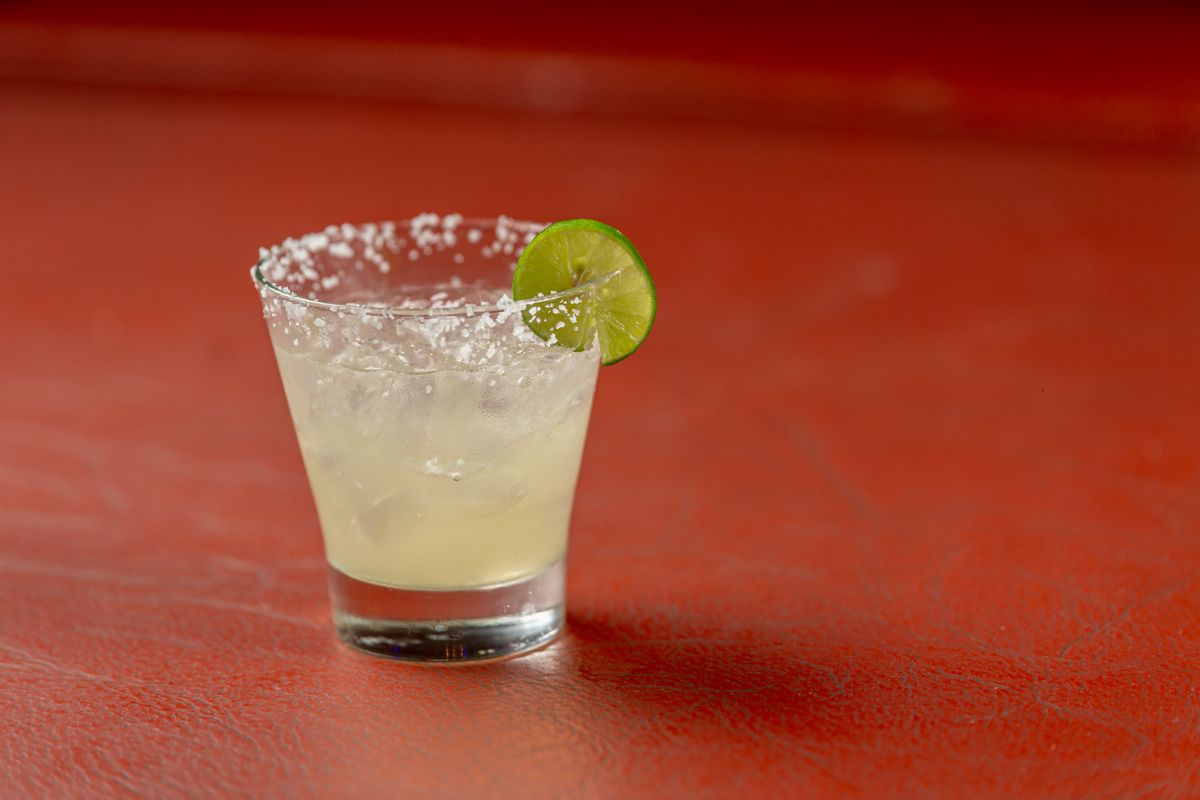 Pale margarita on the rocks in a salt-rimmed glass with a lime wheel on red
