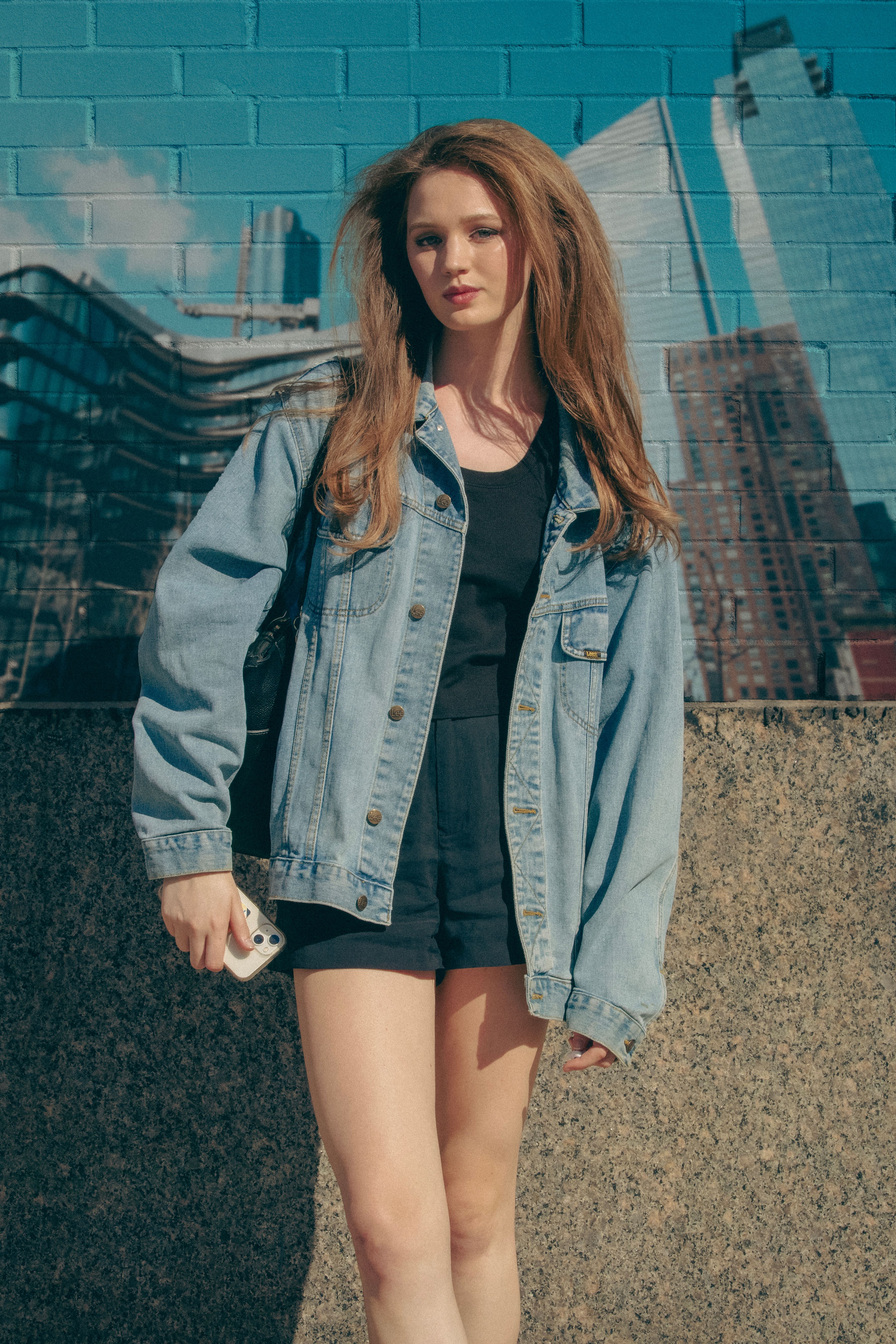 Stylish young woman in denim jacket posing in New York City with skyscrapers in the background.