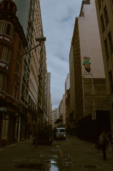 Narrow city street bordered by tall buildings with street art and a distant vehicle, reflecting urban life.