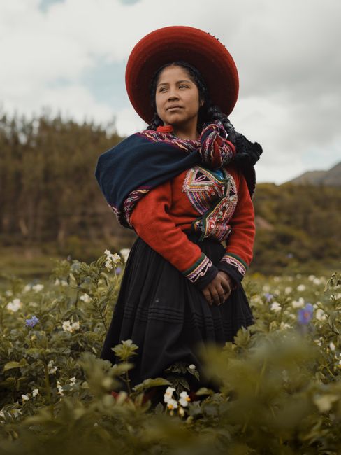 A Latina woman in traditional Peruvian attire stands in a Cusco field, showcasing cultural heritage.