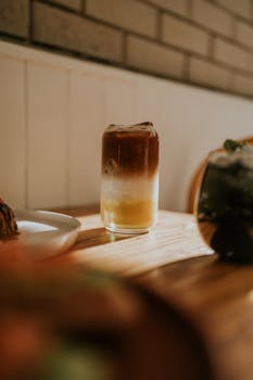 Close-up of an iced coffee on a wooden table bathed in warm sunlight.