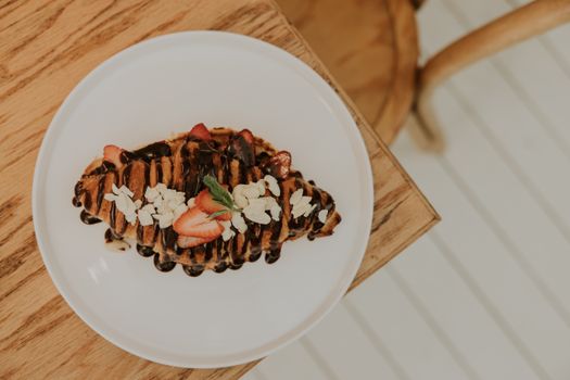 Top view of a chocolate drizzled croissant garnished with strawberries and almonds on a white plate.