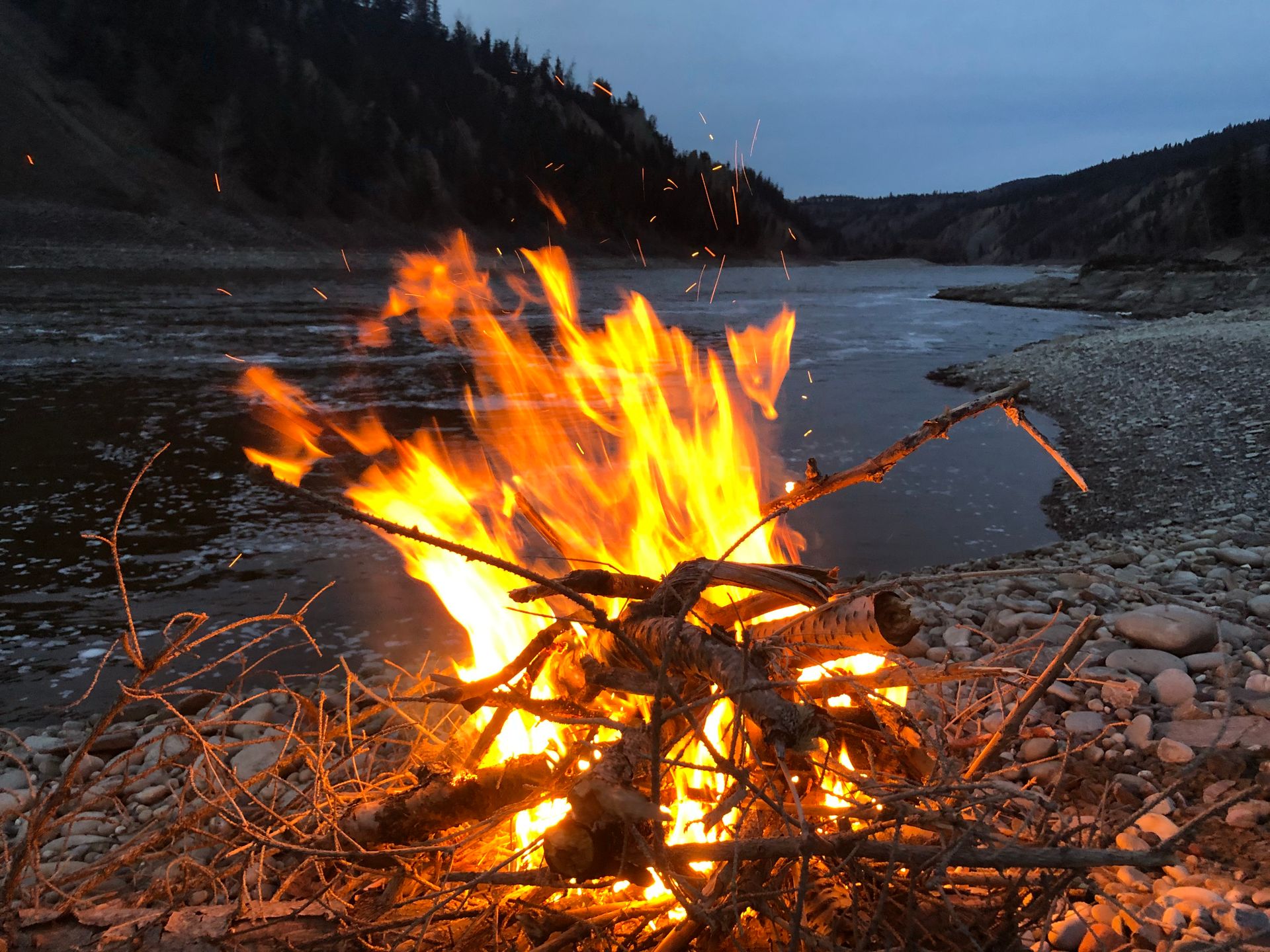 Vibrant bonfire near Williams Lake, BC, surrounded by river and twilight scenery.