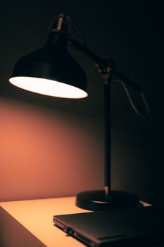 Elegant desk lamp illuminating a closed laptop on a desk, creating a warm and cozy atmosphere.