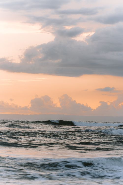 Free Serene Bali coastline at sunset with dramatic clouds and calming waves. Stock Photo