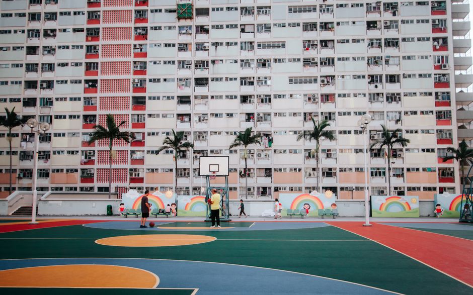 Colorful basketball court in front of high-rise apartments with palm trees and rainbow mural.