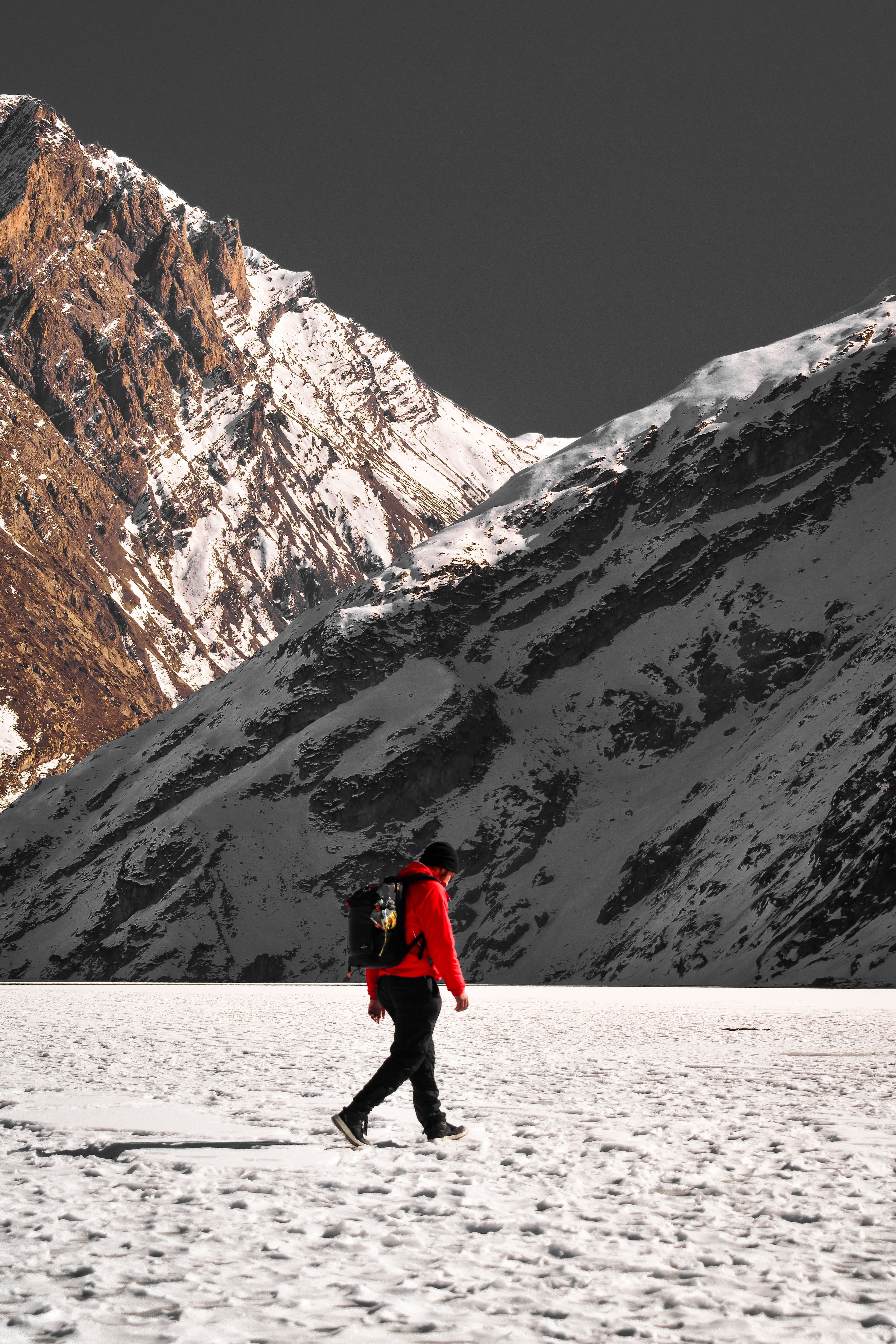 Solo hiker in red jacket exploring snowy mountain terrain during winter, showcasing stunning scenery.