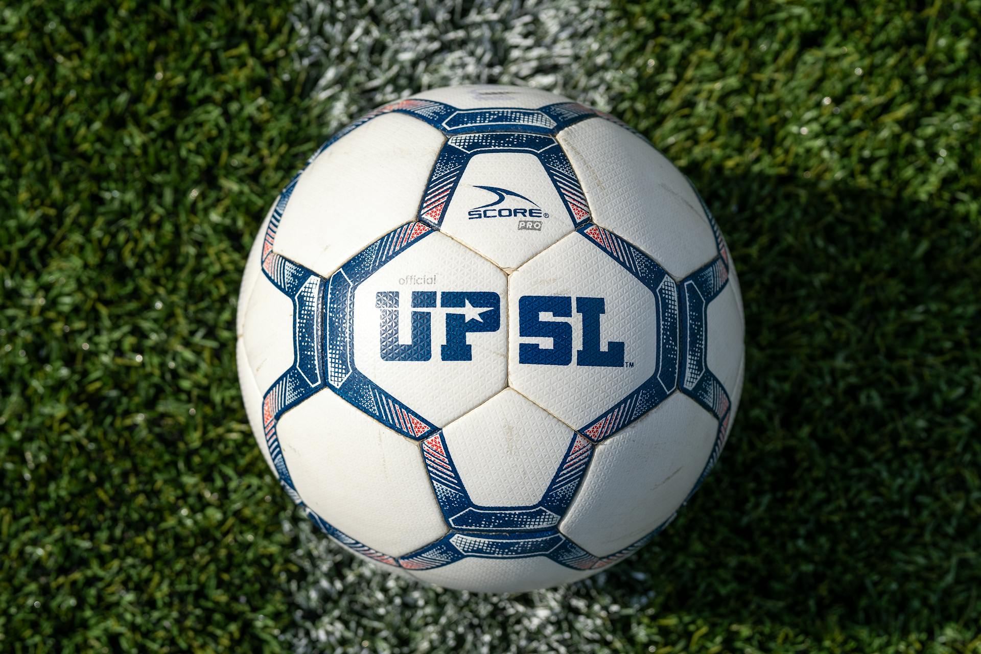 Official UPSL soccer ball resting on green artificial turf field, showcasing sports equipment.