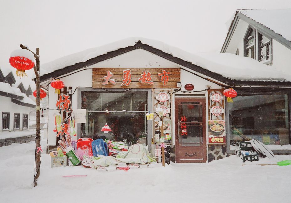 Charming snowy village store with Asian architecture and red lanterns in winter setting.
