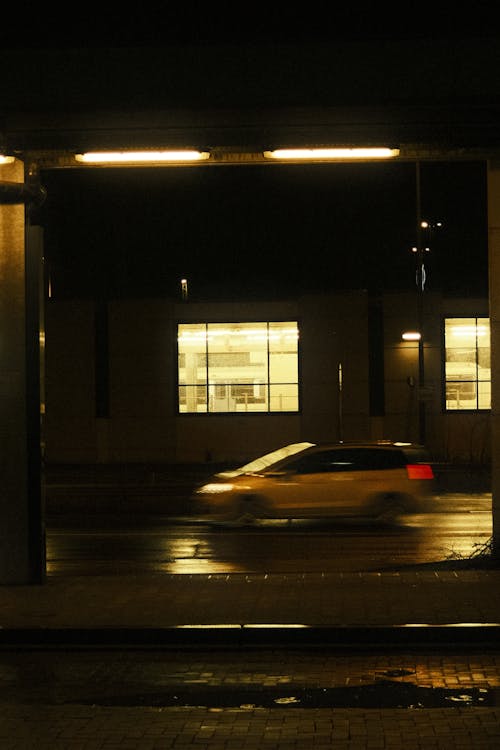 A Car in Blurred Motion on a Street near a Building at Night 