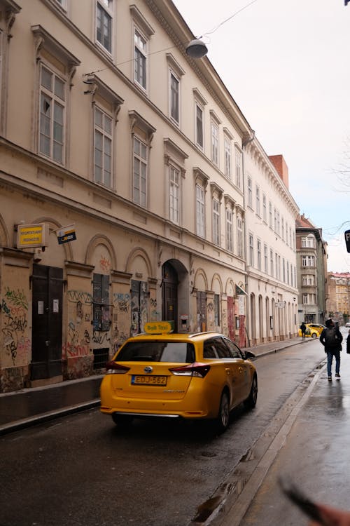 A Yellow Car Driving on a Street by a Building in City 