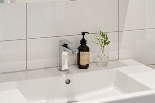 Close-up of a Bottle of Soap and a Small Vase with a Flower Standing on a Sink 