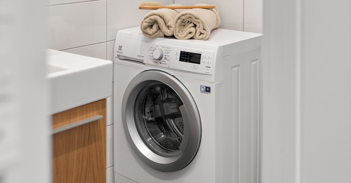 Witte wasmachine met opgerolde handdoeken erop in een lichte washoek