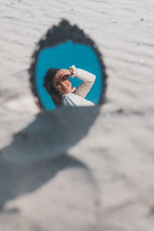 Free Creative reflection of a young woman in a mirror on a sunny beach, capturing a playful moment. Stock Photo