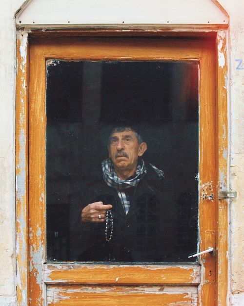 Free Elderly man with mustache gazing through old wooden glass door with prayer beads in hand. Stock Photo