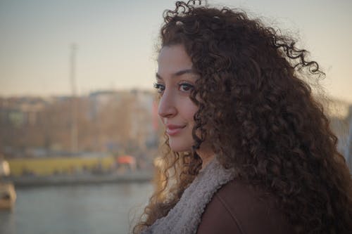 Young Woman with Curly Hair Standing near a Body of Water 