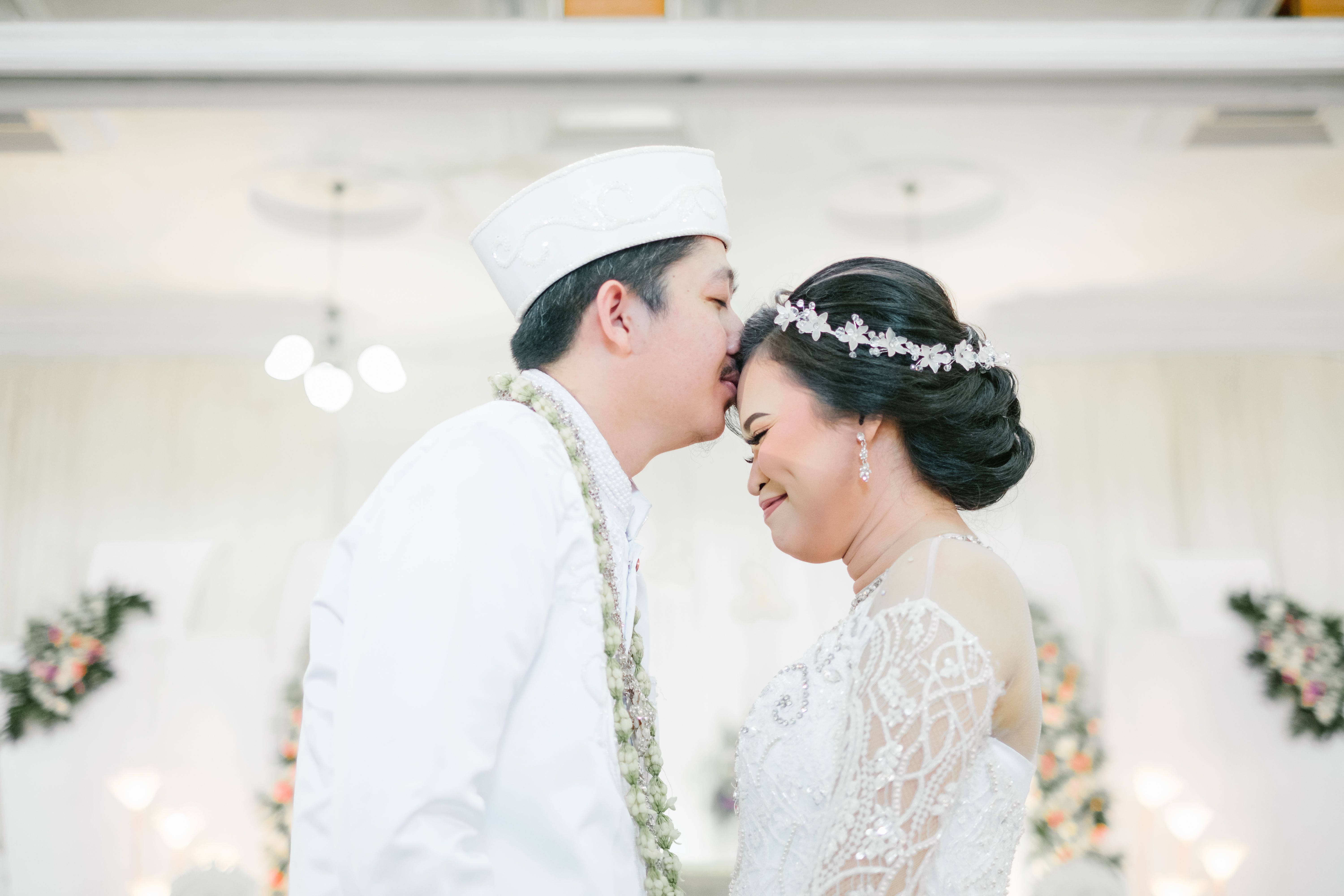 Bride and groom sharing a tender forehead kiss during a wedding ceremony.